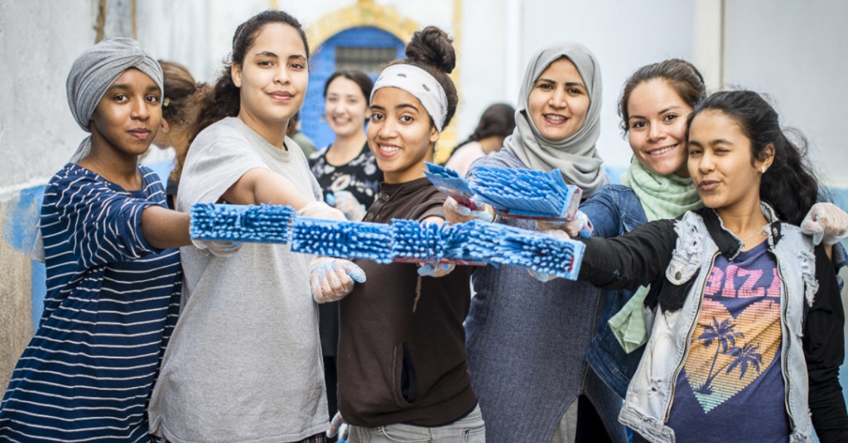 Girls smile holding paintbrushes with blue paint on them. avoid funding hate and extremism.