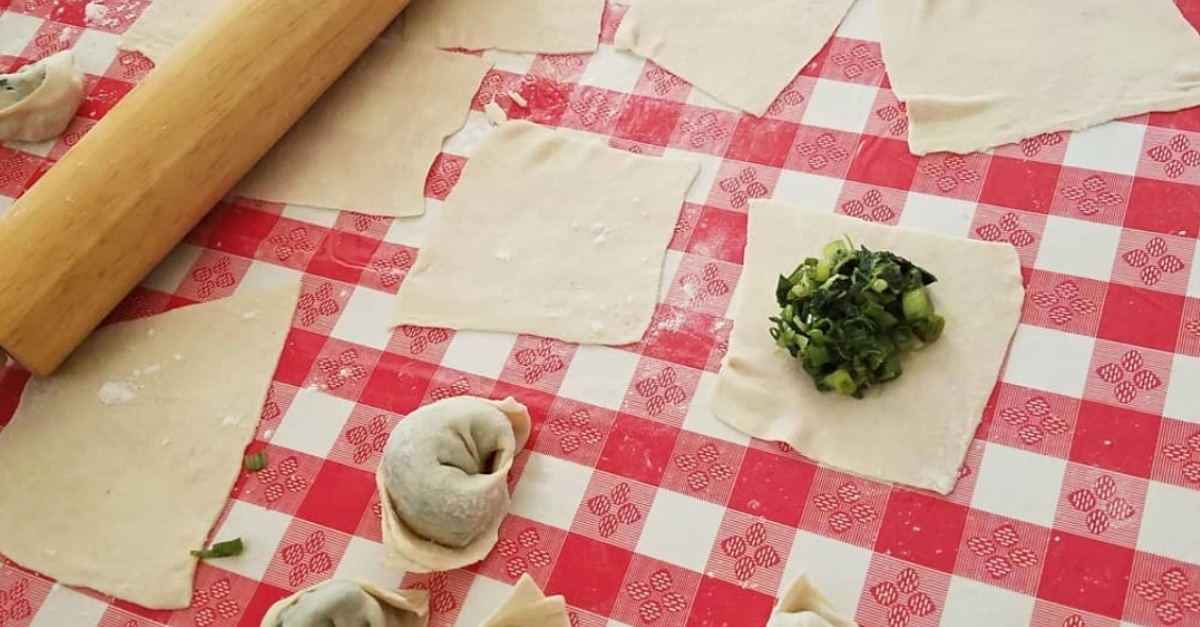 Squares of dough and filling on a red plaid tablecloth. A rolling pin sits in the corner