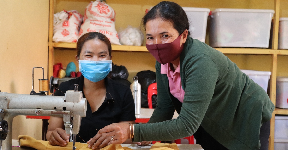 Two women wearing face masks smile while working together near a sewing machine. One holds thread in her hand. Implicit bias in philanthropy