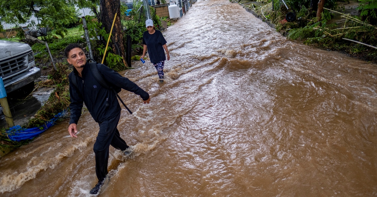 Two people wade through brown water on a flooded street in the aftermath of Hurricane Fiona in Salinas, Puerto Rico