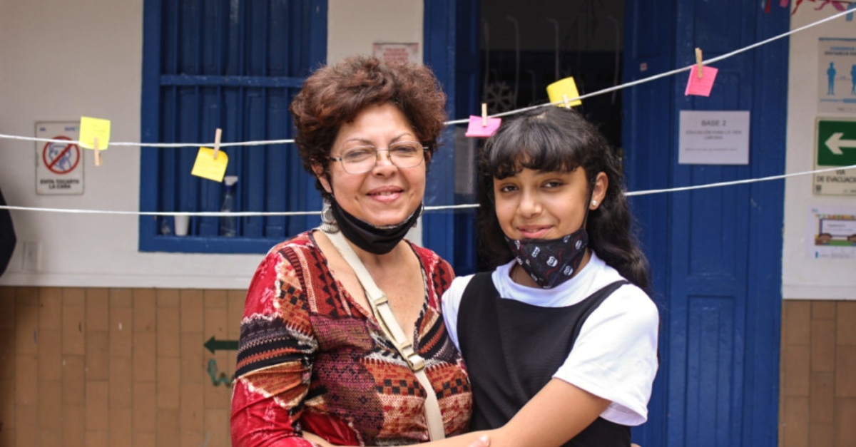 A woman and a young girl stand together in front of a clothesline with notes pinned to it.