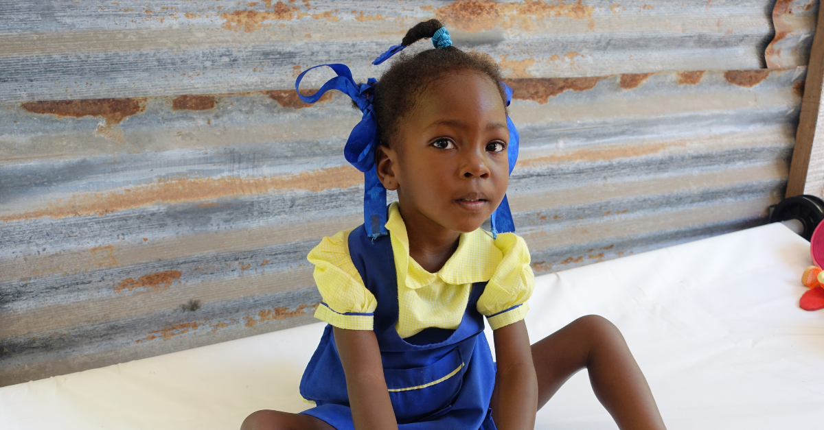 Young girl with pig tails and ribbons in her hair sits on a table.