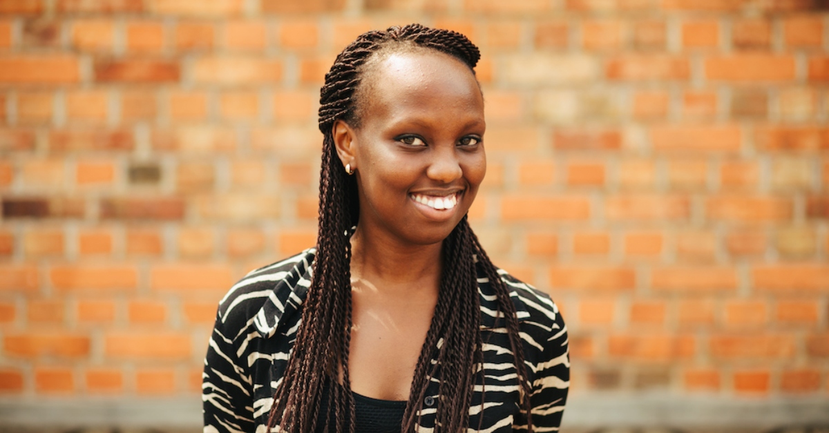 A woman wearing a black and white jacket smiles. A brick wall is out of focus behind her.