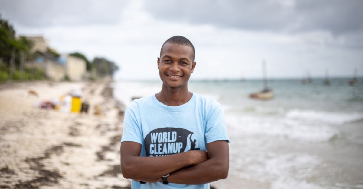 A young person wearing a blue t-shirt smiles. A beach is out of focus in the background. corporate social responsibility articles 2022.