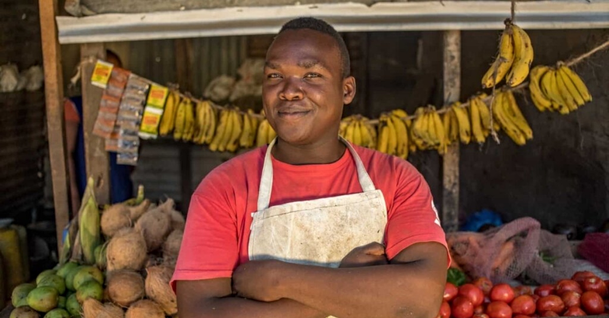 Man smiles at camera, arms crossed, standing in front of market station. 2022 for donors