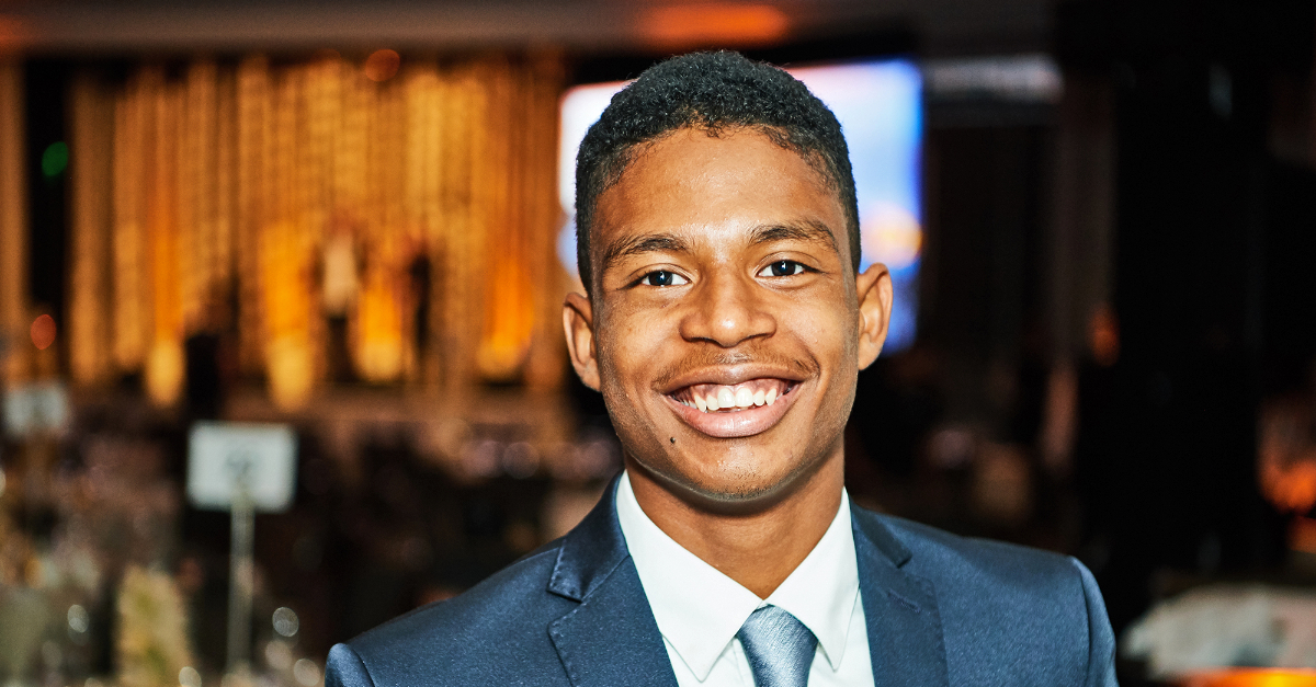 young man in suit smiles at camera, conference room in the background