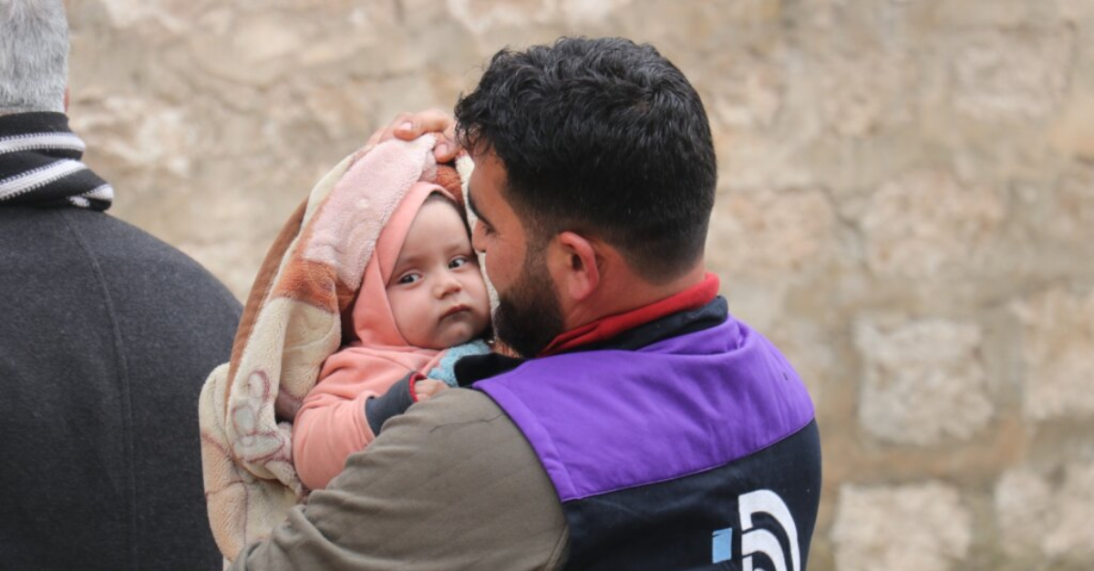 Infant is wrapped in a blanket and cradled by rescue worker. Syria recovery