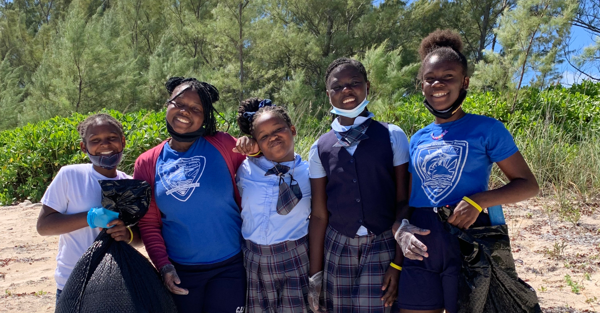 group of students smile and hold up bags of beach litter they've cleaned up