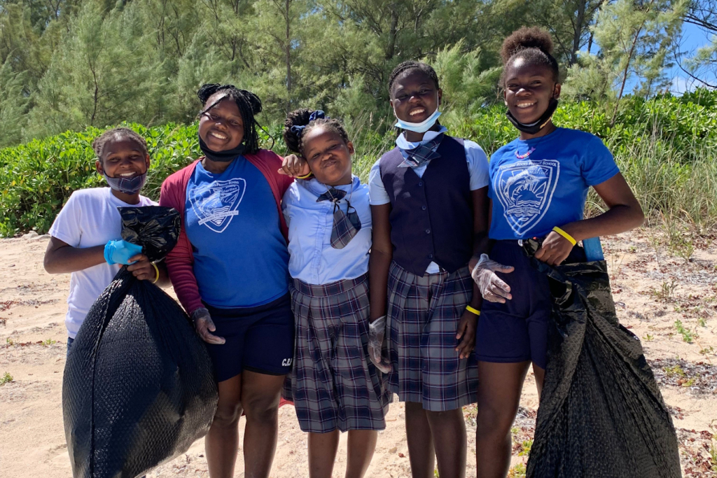 Kids smile at the camera while holding trash bags at a beach cleanup