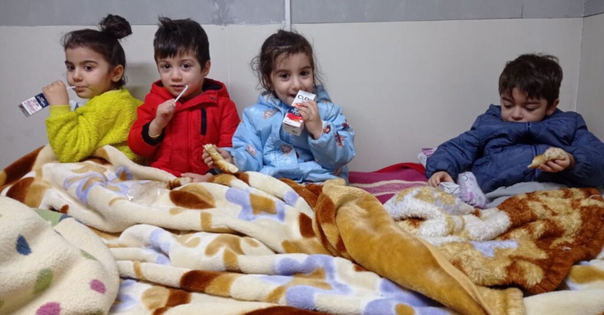 Young children sit underneath a blanked holding juice boxes. How to help turkey earthquake survivors.