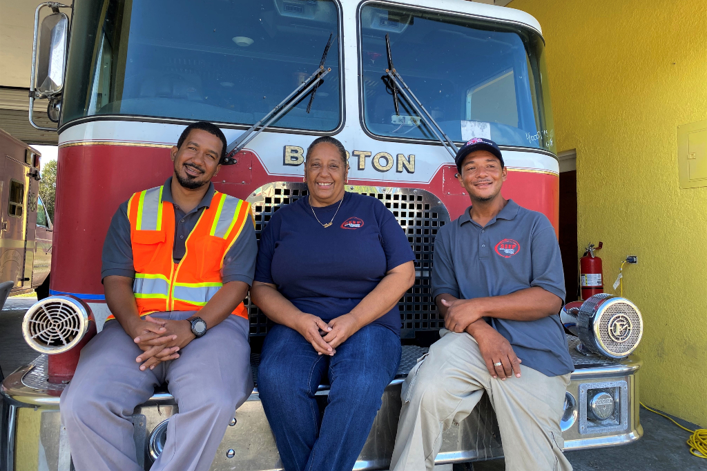 Three workers sit on the bumper of a fire engine after hurricane dorian