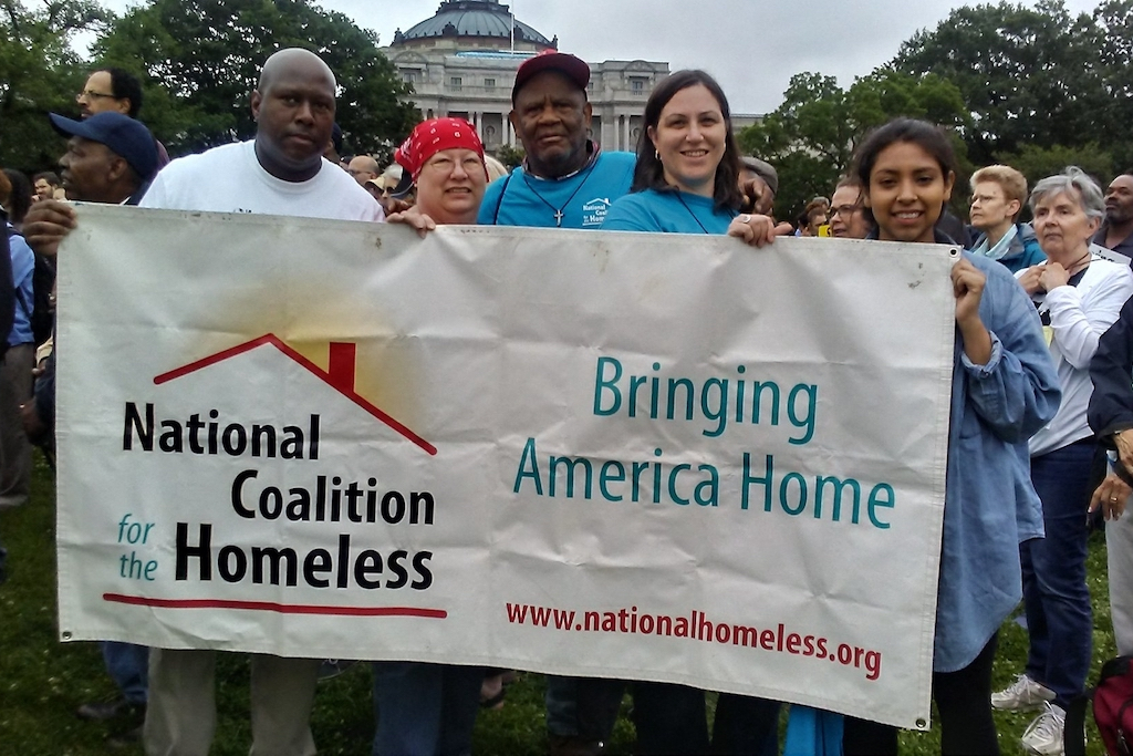 A group of people stand in front of the White House holding a banner for the Bring America Home Now project of the National Coalition for the homeless