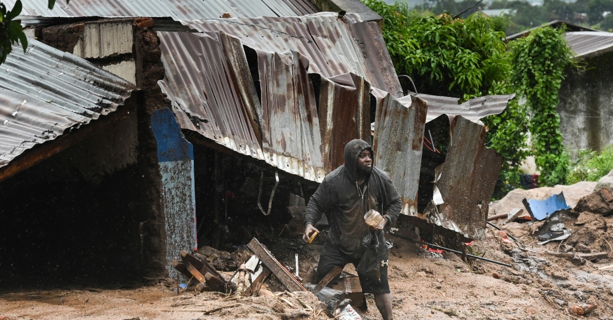 person stands in front of collapsed building, destroyed by cyclone freddy