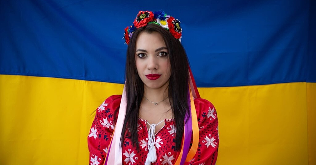 Woman in traditional Ukrainian dress stands in front of Ukrainian flag. tennis plays for peace