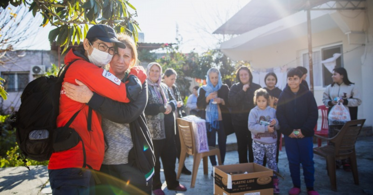 Family stand in background, woman hugs relief worker donate to turkey and syria earthquake