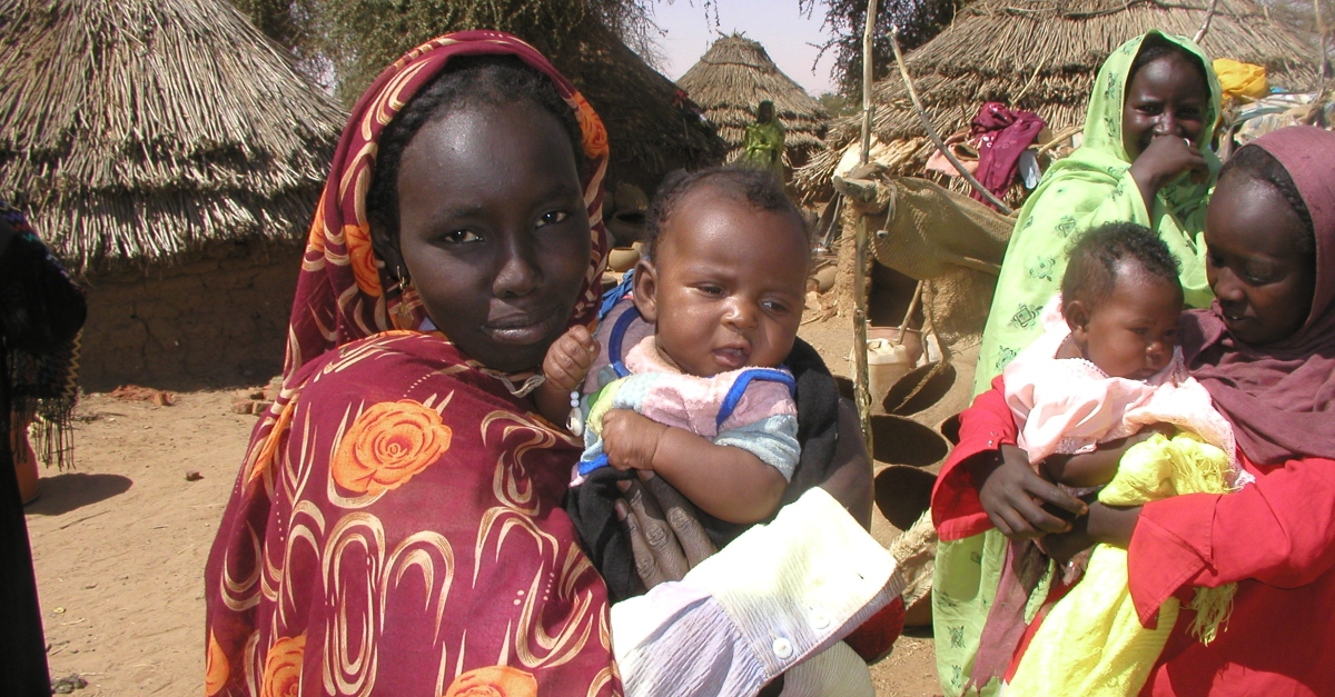 hurricane florence case study A woman holds a baby in the Darfur region of Sudan. Other women with children and mud structures are in the background.