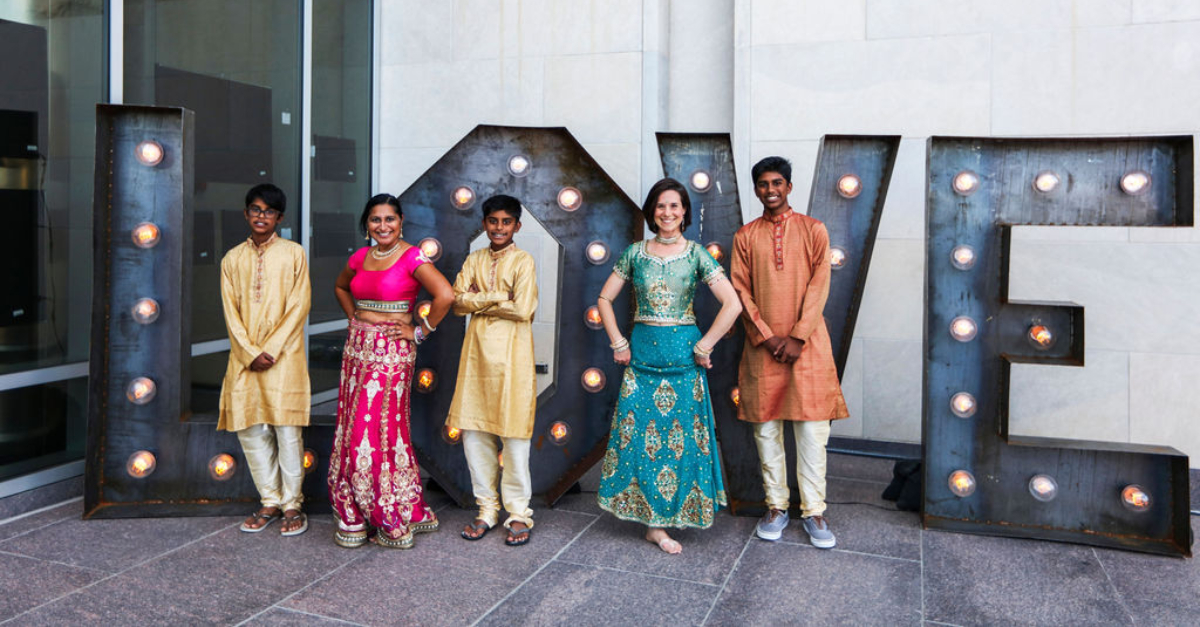 Five people dressed in celebratory Indian dress stand in front of giant letters L O V E wedding charity registry