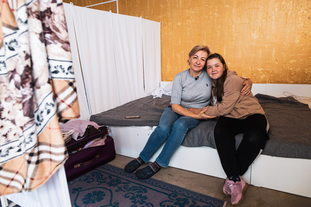 mother and daughter sit on a bed in a dorm and hold each other