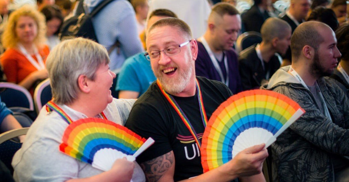 two people sitting in conference hall holding rainbow colored fans LGBTQ+ equality