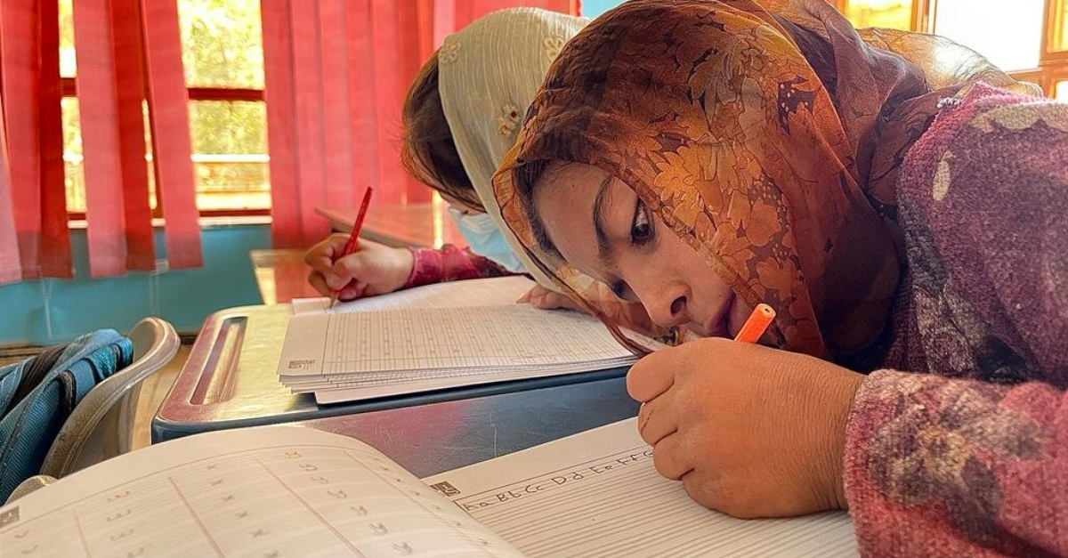 girl sits at schoolhouse desk writing intently education in afghanistan