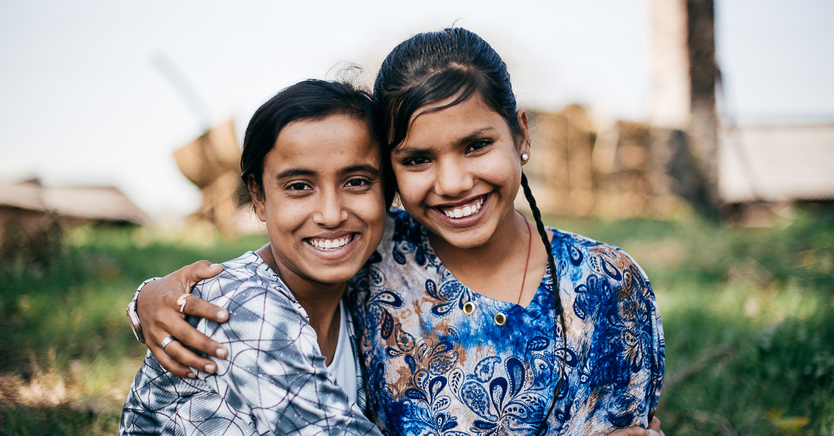Two people smile while embracing. A field and structures are out of focus behind them. Charitable appreciation gifts