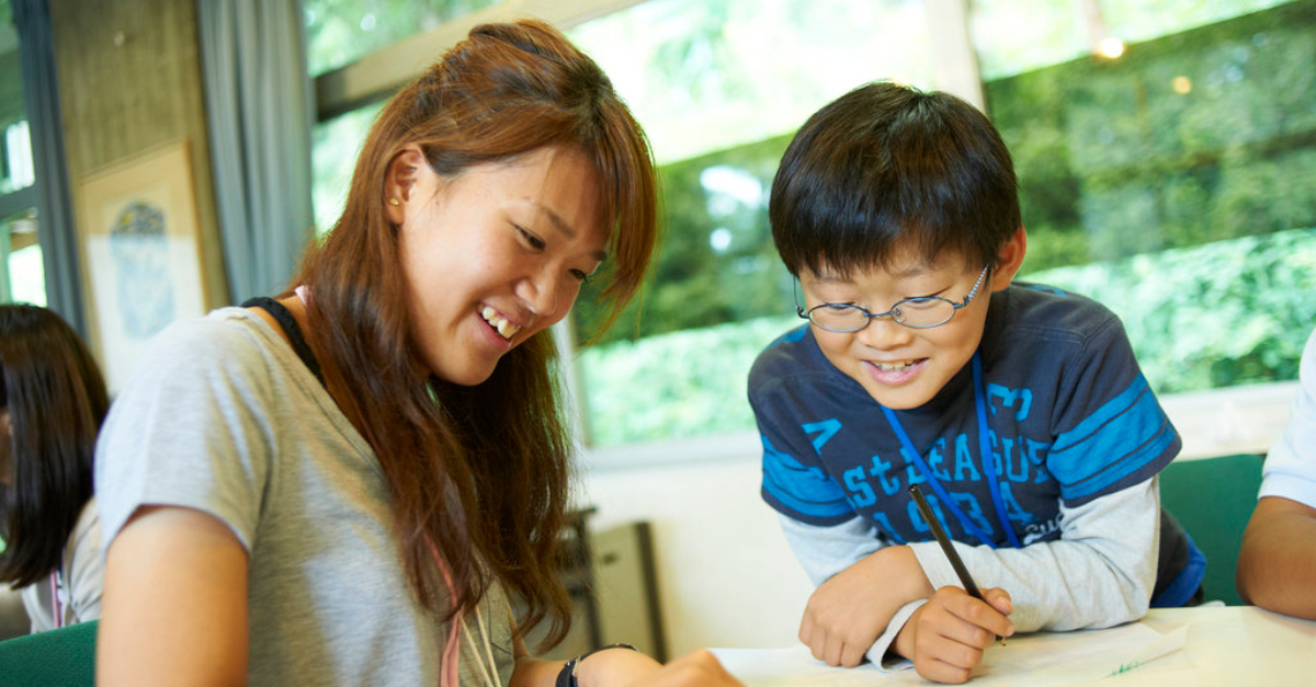 Young woman and boy smile while writing something together at a desk. Flexible grantmaking