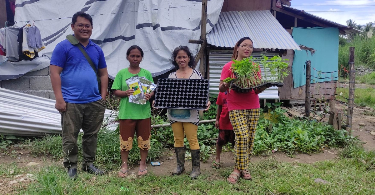 Four smiling people face forward, three hold farm inputs like trays and seedlines in their hands.