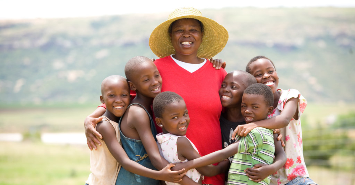 children hug a woman who is wearing a sun hat, everyone is smiling at the camera