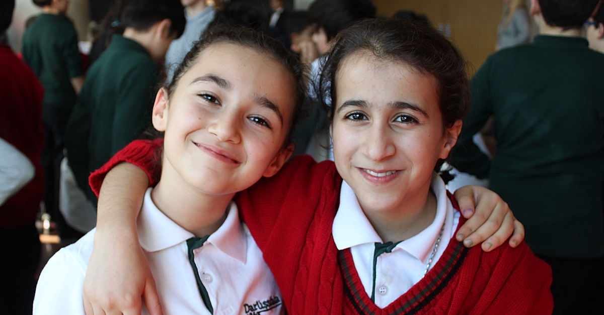 two schoolgirls stand together smiling at the camera how do I give my QCD to charity