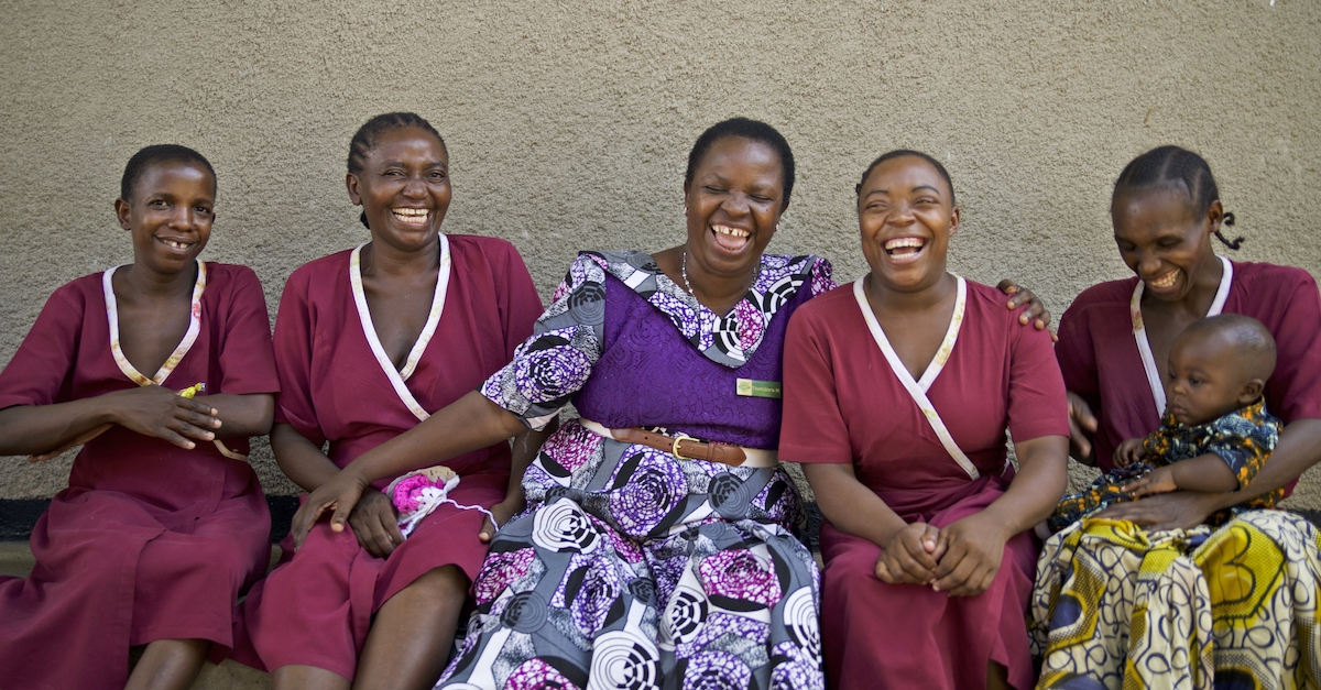 Five women sit together smiling and laughing, one of them has a baby on her knee. community-led initiatives