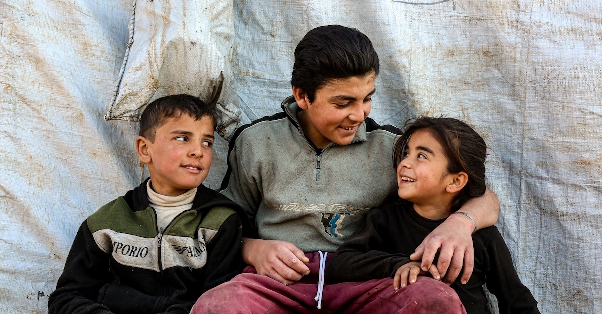 the next generation of generosity three children sit in front of a tarp smiling at each other