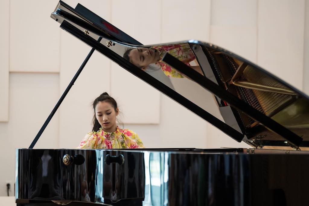 woman sits behind a baby grand piano