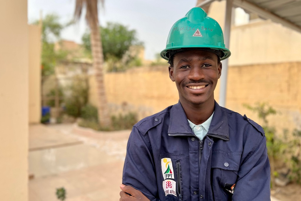 young man wearing safety hat and uniform crosses arms and smiles at camera