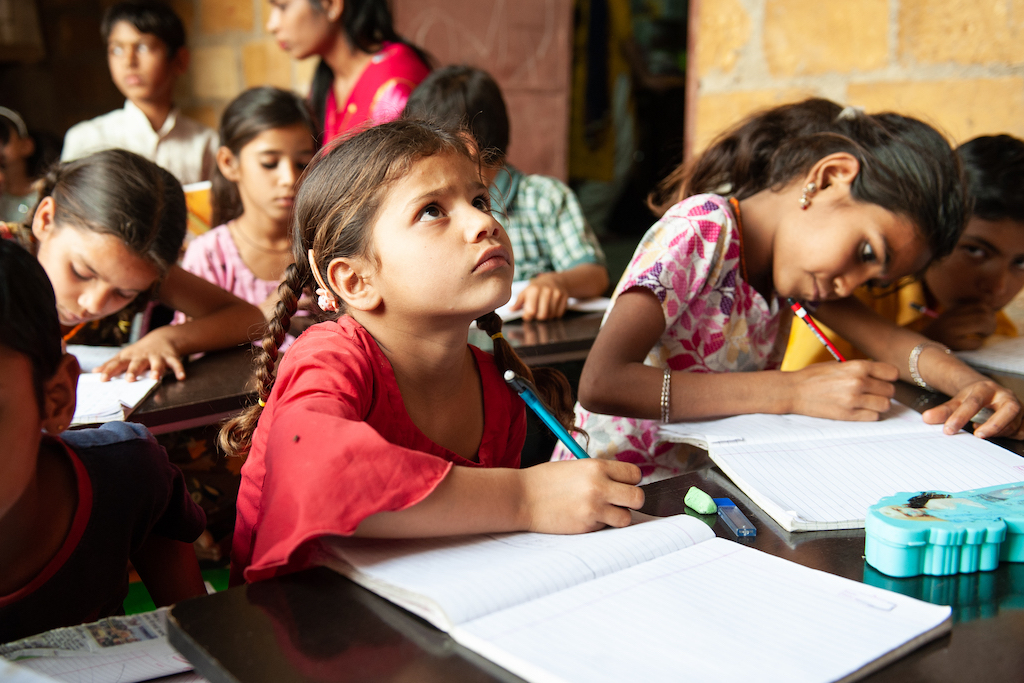 girl looks up quizzically as she sits at her desk in a classroom filled with students inspiring nonprofit photos of 2023