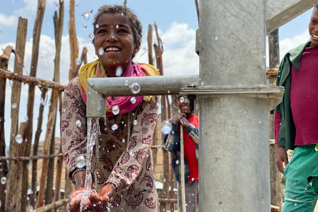 girl holds her hands under an outdoor well pump inspiring nonprofit photos of 2023