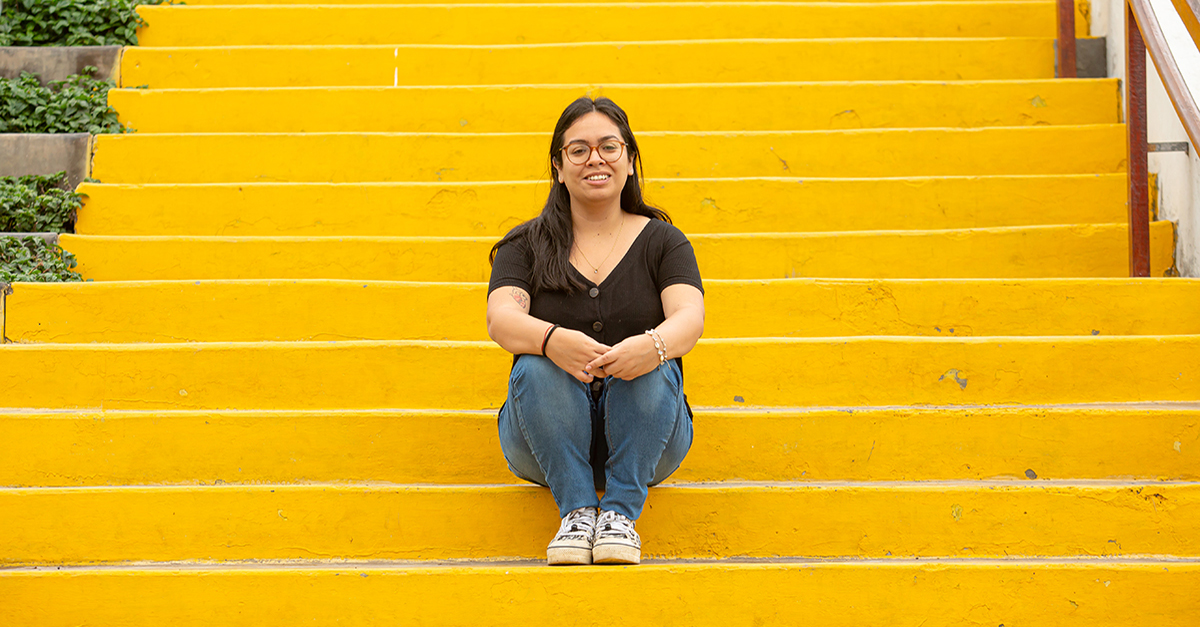 GlobalGiving Community Voices Fellow Paloma Rodríguez sits on a yellow staircase with her hands crossed over her knees in Peru.