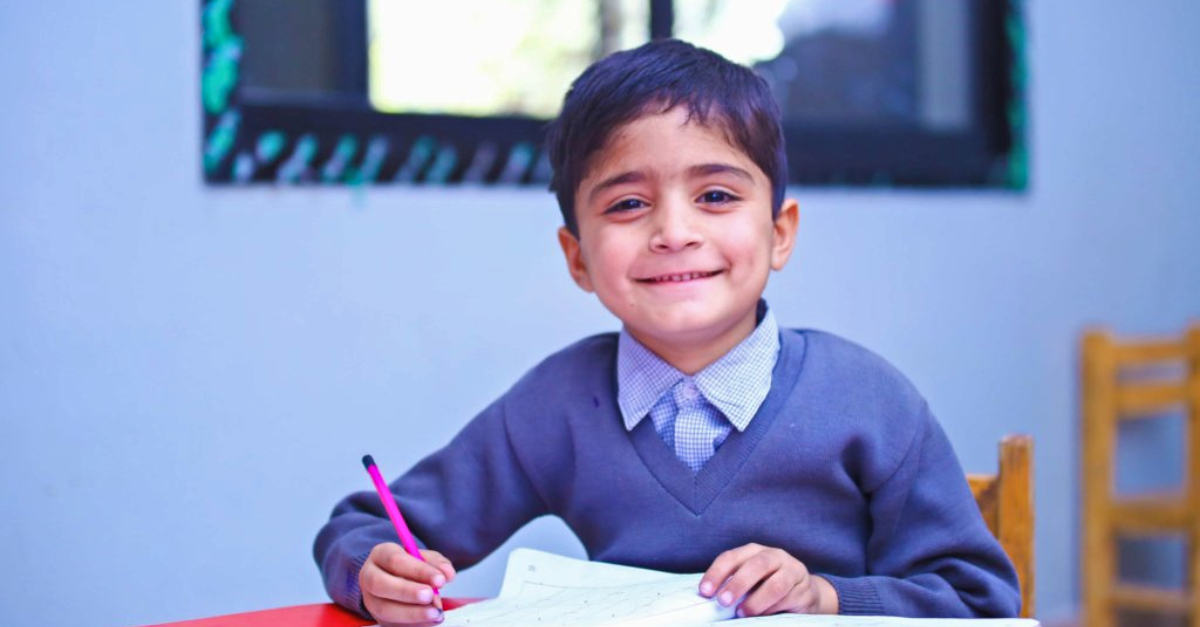 schoolboy sits at desk and looks up from paper, smiling the impact of compassion