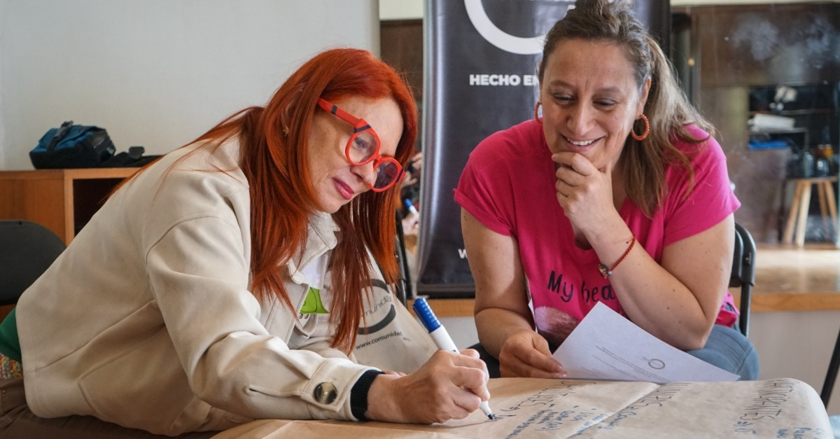 Two smiling women in an office write ideas on a large sheet of paper