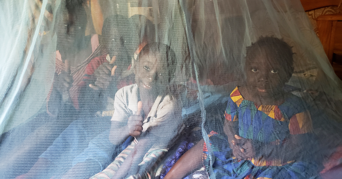 A family poses underneath a mosquito net, giving the thumbs up sign. Photo by Develop Africa, Inc.