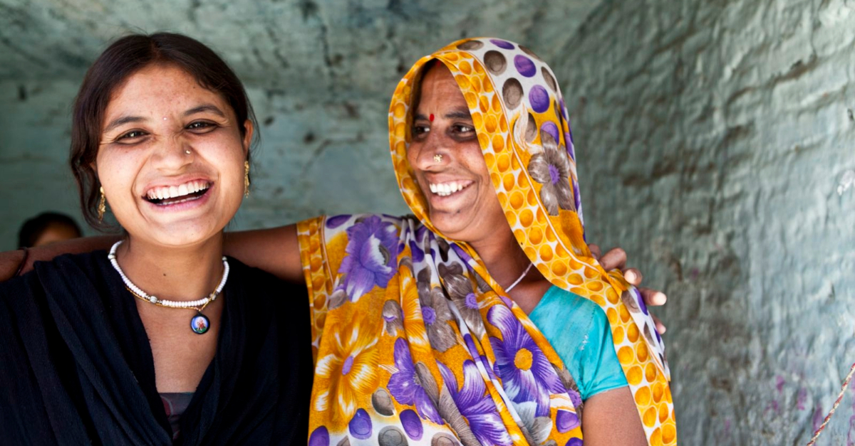 Two women smiling, one facing the camera and one facing the other woman.