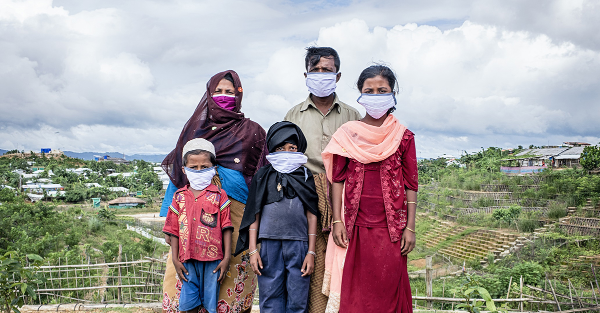 A Rohingya family poses against a blue sky and grassy hills. Photo by GlobalGiving Partner Action Aid USA