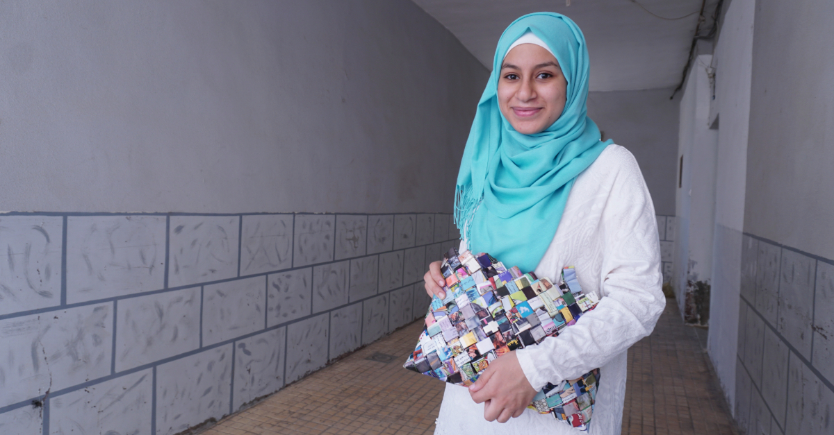 Girl stands to the right smiling and holding a colourful bag
