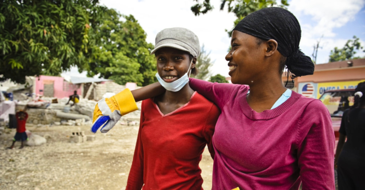 One woman faces the camera smiling with another woman stood with her arm around her and smiling at her