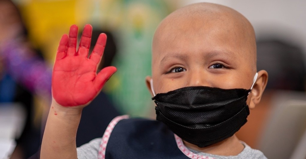A young child with a mask waves to the camera during the COVID-19 pandemic.