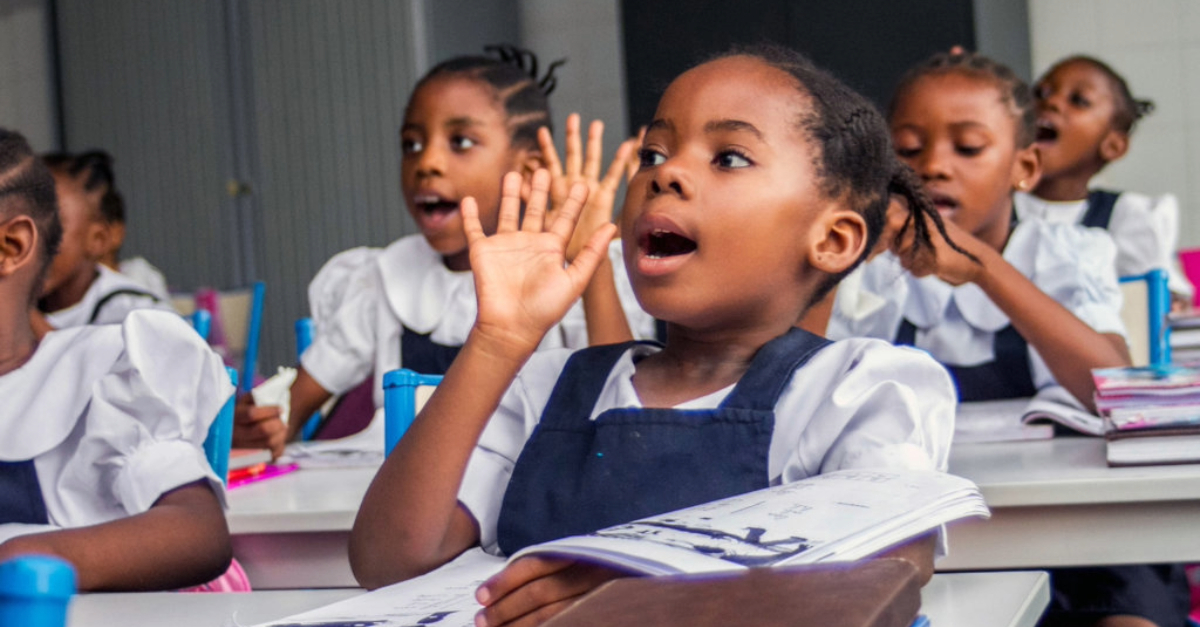 Young girl energetically calls out in class surrounded by engaged peers
