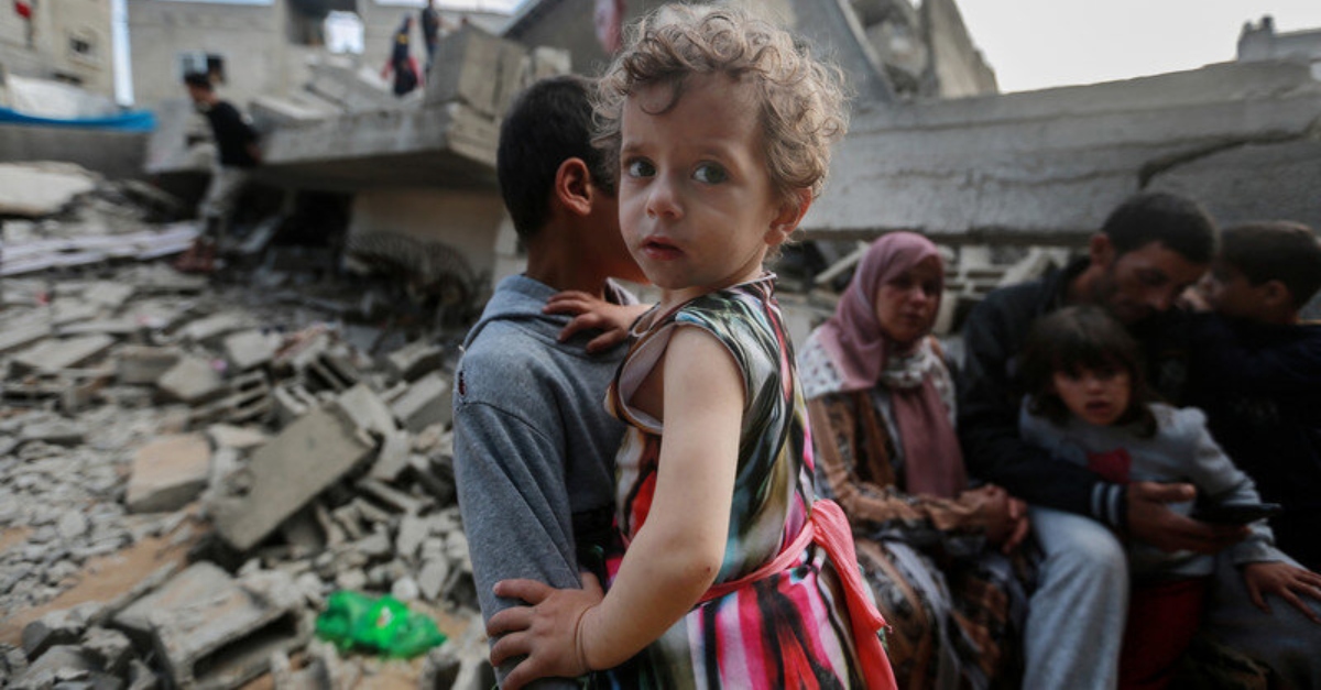 A child photographed in front of destroyed homes and buildings in Palestine.