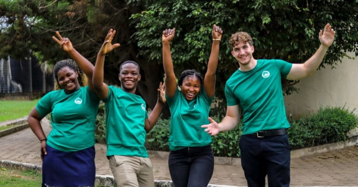 Four young adults are raising their arms in celebration and smiling at the camera.