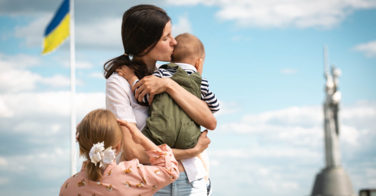 A mother holds her children in front of a Ukrainian flag