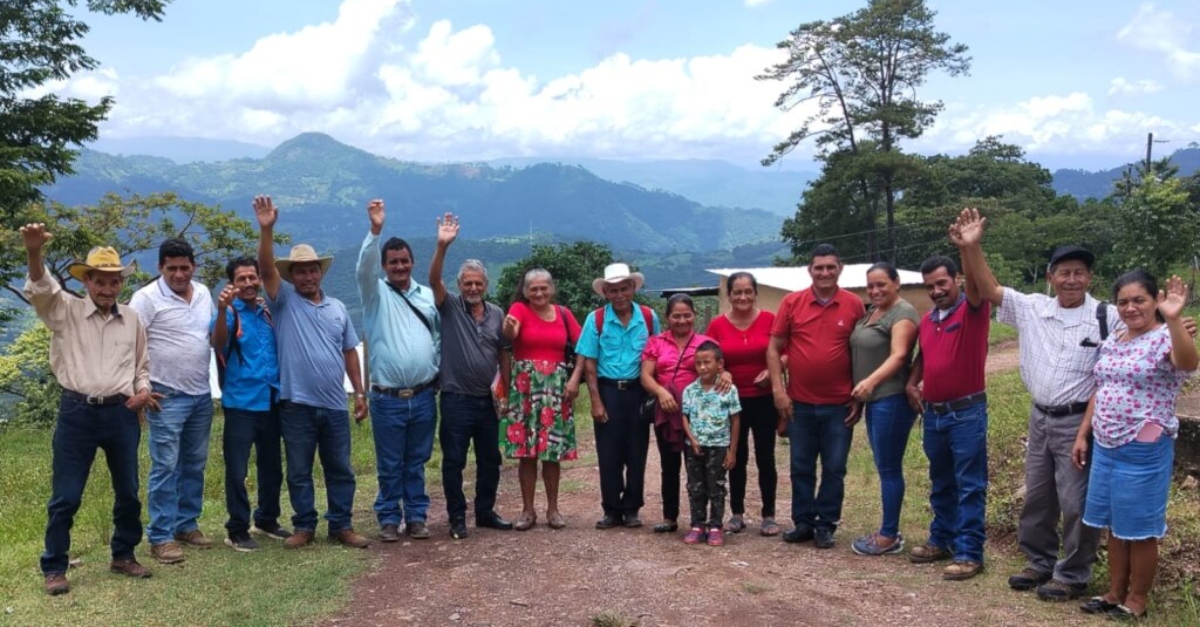 Around 20 people Indigenous community members and farmers waving to the camera in front of mountains in Honduras