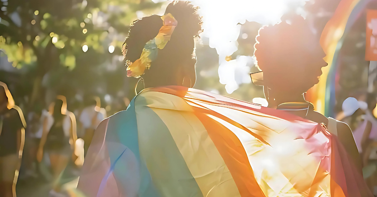 Two community members wrapped in an LGBTQ+ rainbow flag at a pride parade